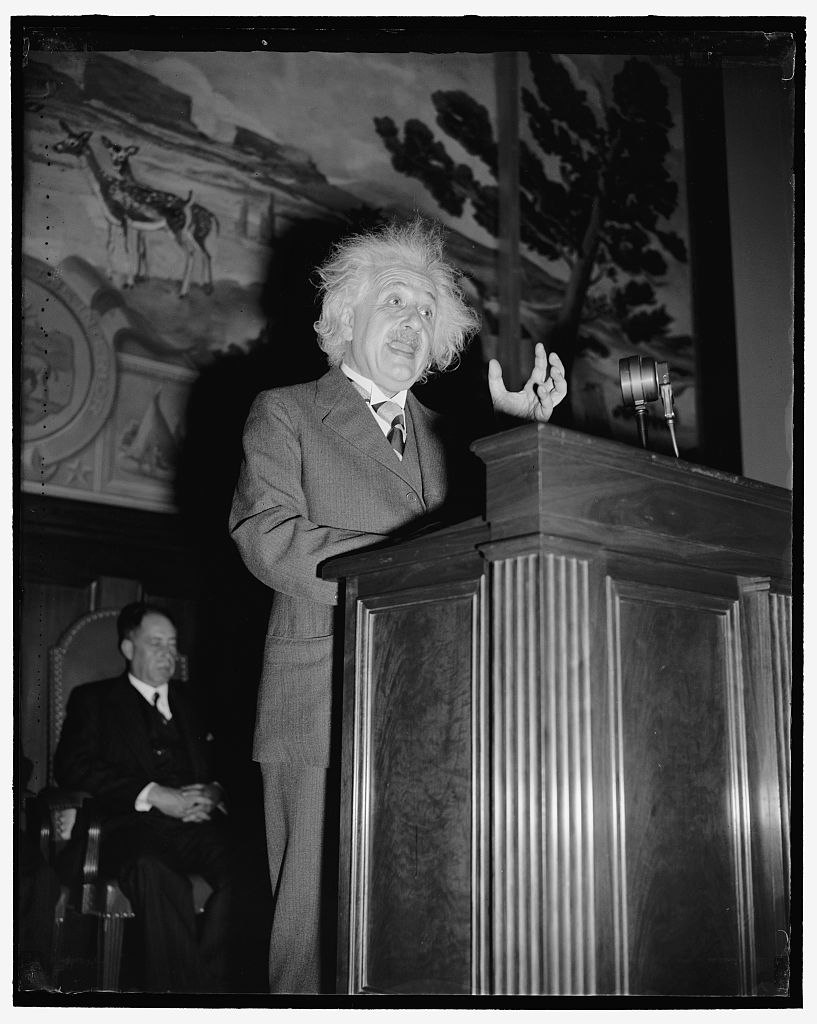 Einstein speaking at a lectern with one finger raised