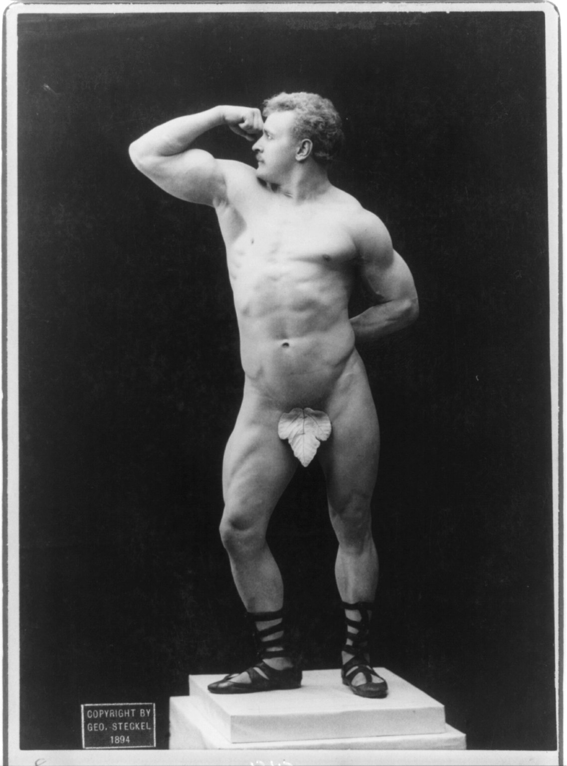 Eugen Sandow in profile flexing his arm in an 1894 studio photograph